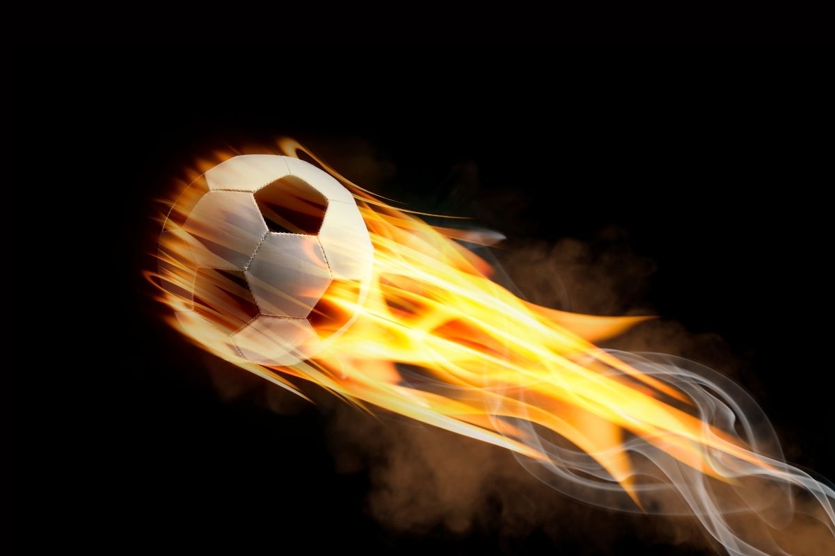 Football engulfed in flames flying across a dark background, symbolizing intense matches, high tempo play and goal-driven football action.