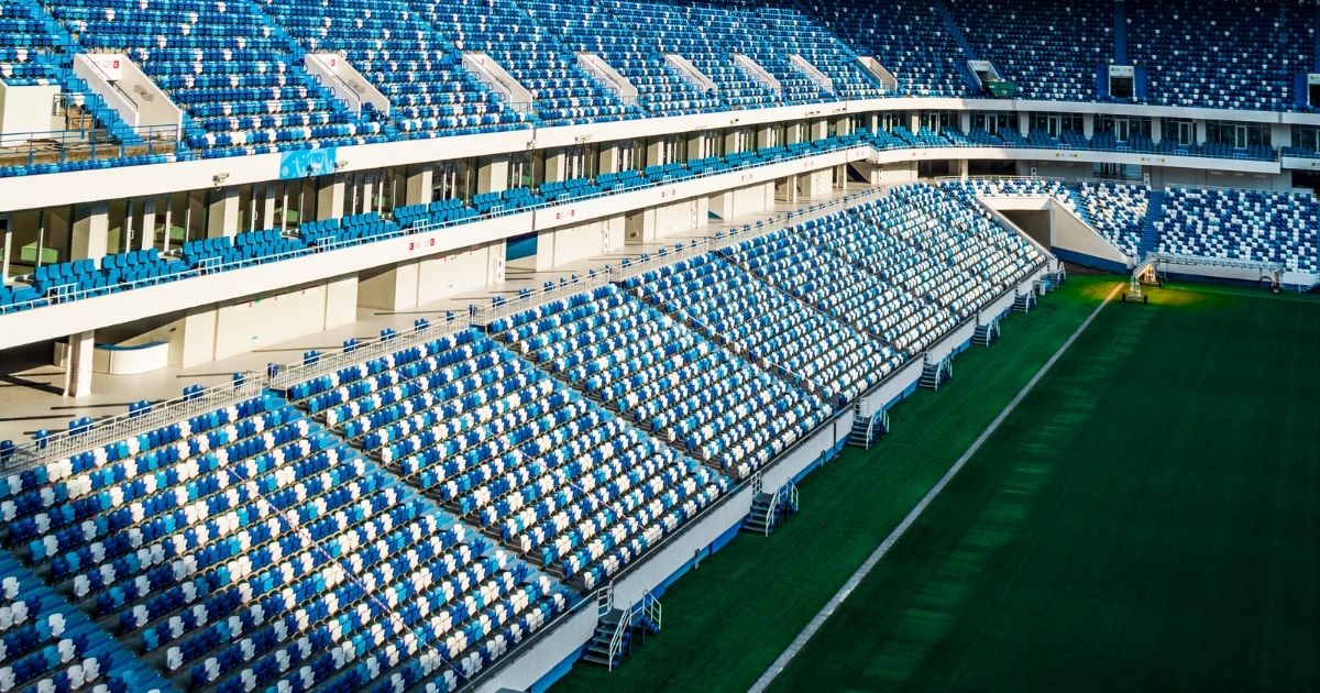 Empty football stadium with blue and white seats viewed from the stands, showing the pitch and seating sections ahead of a matchday atmosphere.