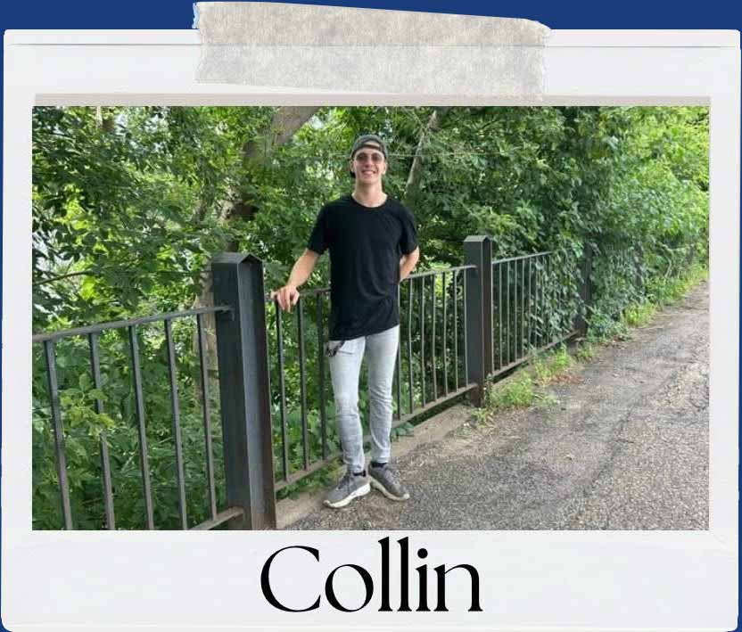 Collin, a young man in a black shirt and jeans, stands on a bridge with lush green trees in the background.
