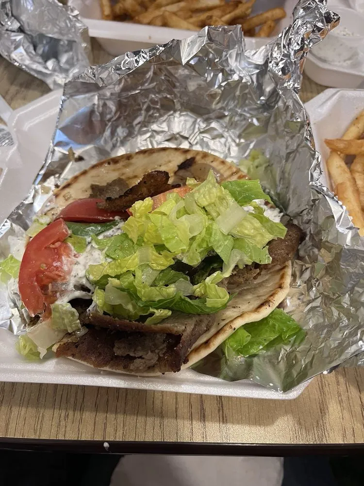A gyro sandwich with lettuce and tomato on a foil wrapper.