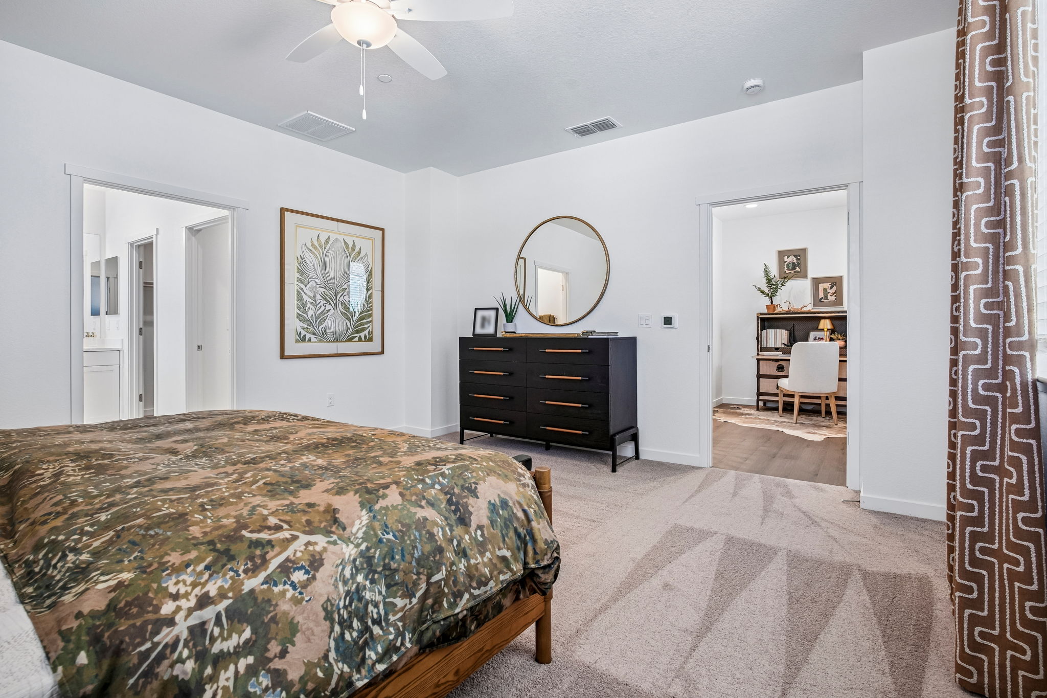 Bedroom with bed, wall art, dresser and view into bathroom and hallway