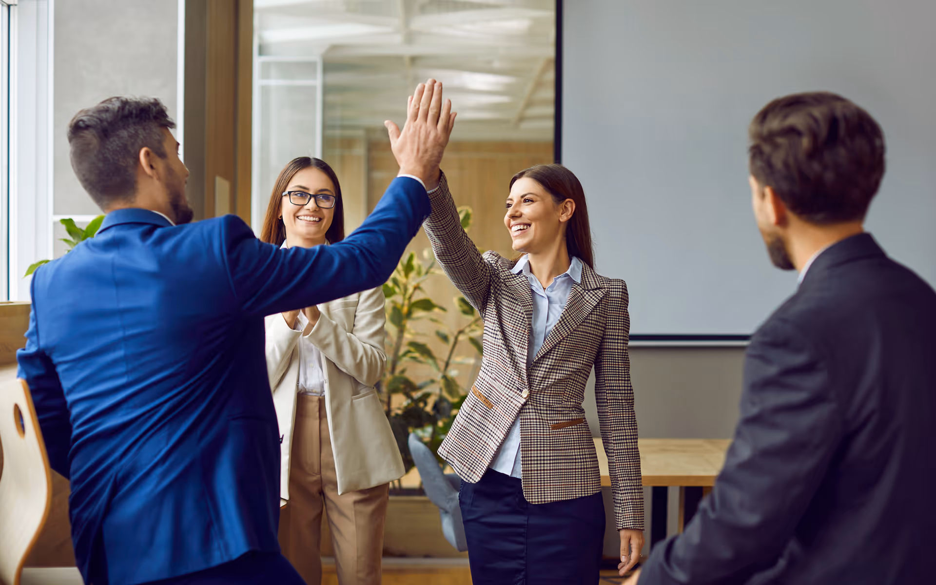 Two business professionals giving a high-five while two colleagues smile and watch in a modern office.