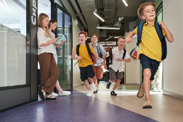 Group of school children running through modern hallway, wearing backpacks and yellow shirts.