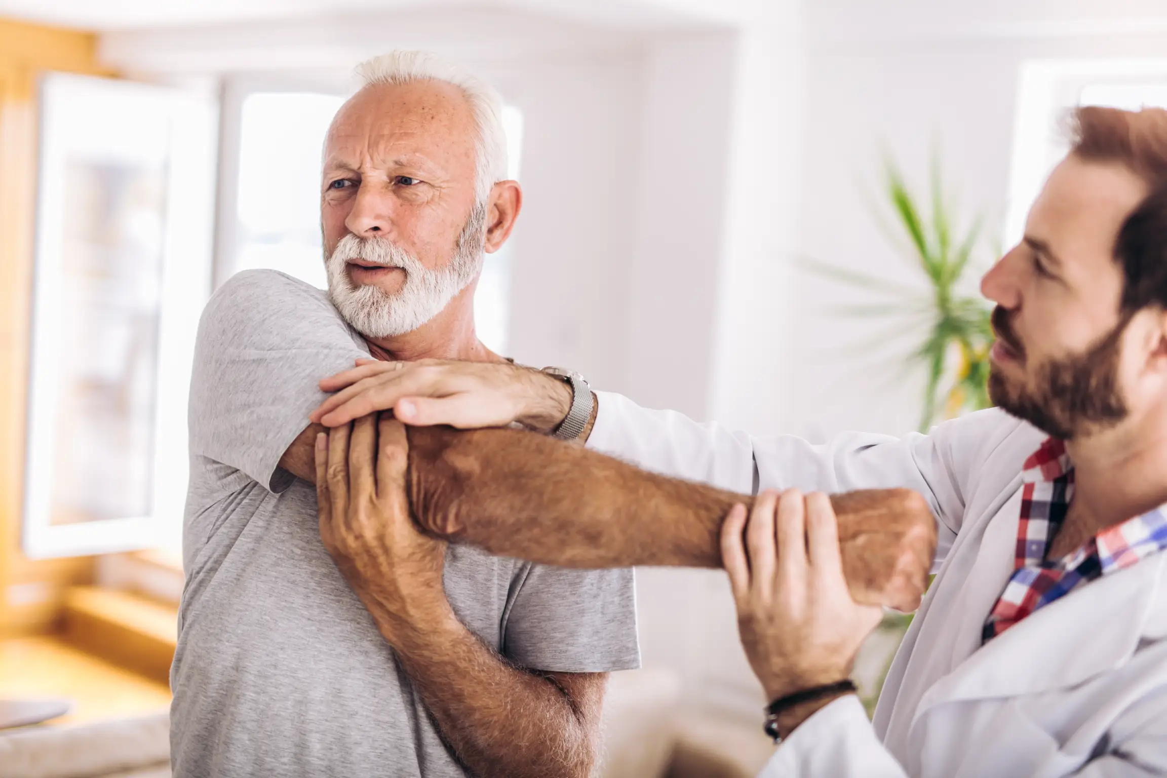 Senior man receiving a physical therapy assessment on his arm by a medical professional in a bright, inviting room.