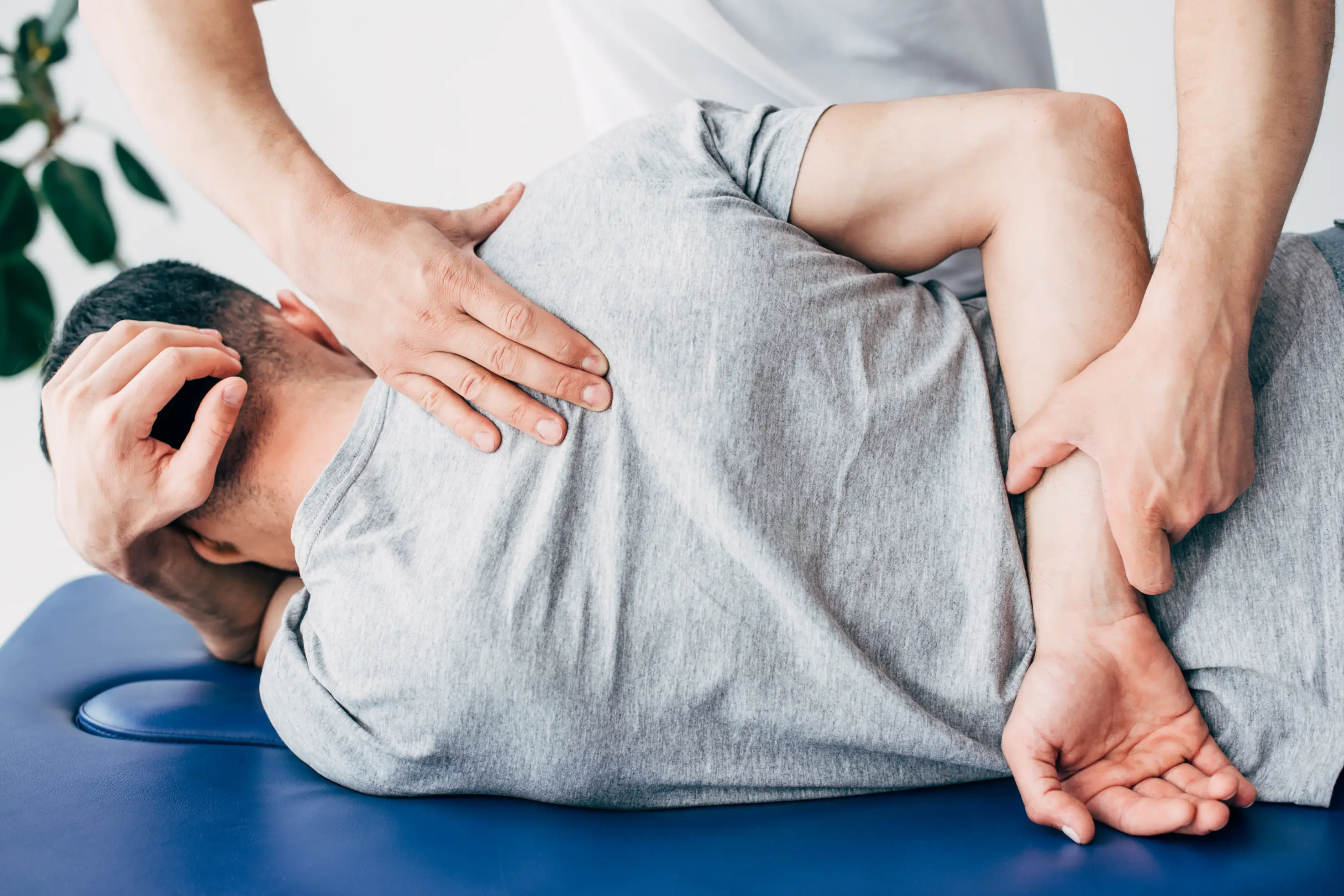 A chiropractor is performing a hip alignment or back adjustment on an elderly patient lying on their side on a treatment table, demonstrating a hands-on therapeutic procedure.
