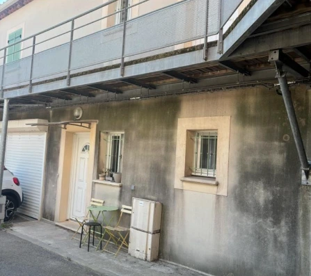 Façade d'une maison avec une porte de garage blanche, deux fenêtres avec barreaux, un volet fermé et un climatiseur mural.