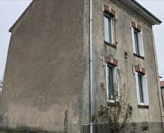 Allée pavée bordée de haies vertes avec une maison à gauche et un van blanc garé au fond sous un ciel nuageux.