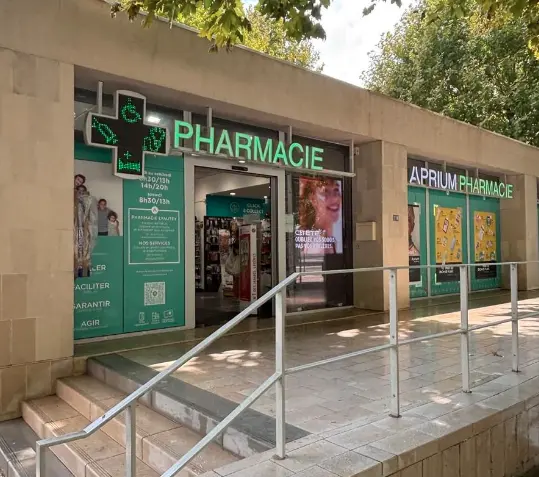 Façade jaune d'une maison avec volets blancs fermés, ombragée par un arbre au feuillage vert sous un ciel bleu avec quelques nuages.
