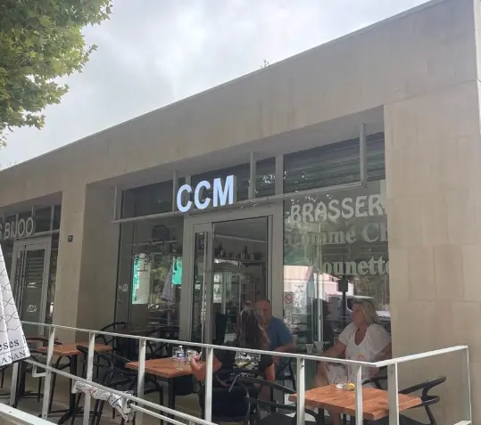 Façade jaune d'une maison avec volets blancs fermés, ombragée par un arbre au feuillage vert sous un ciel bleu avec quelques nuages.