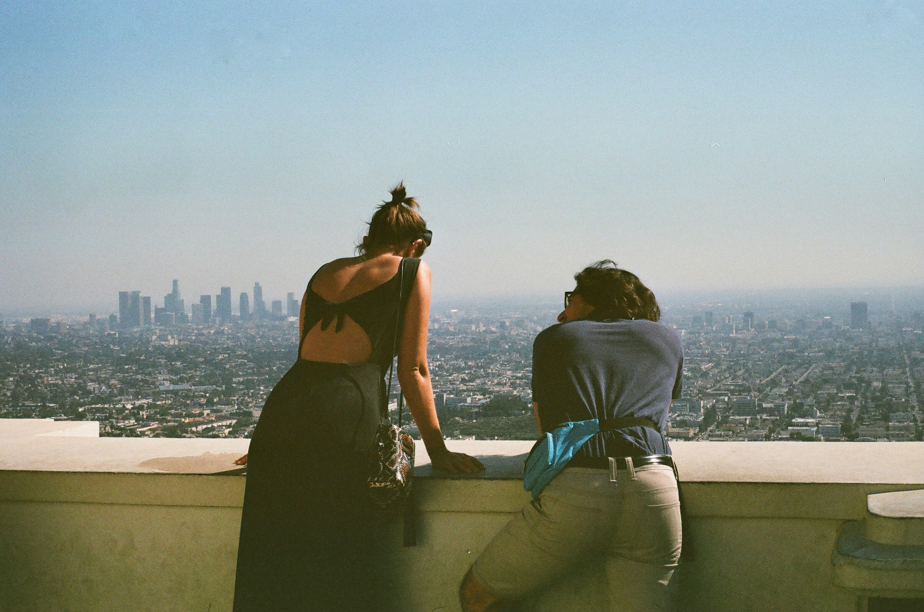 Two people leaning on a ledge overlooking a sprawling cityscape under a clear sky.