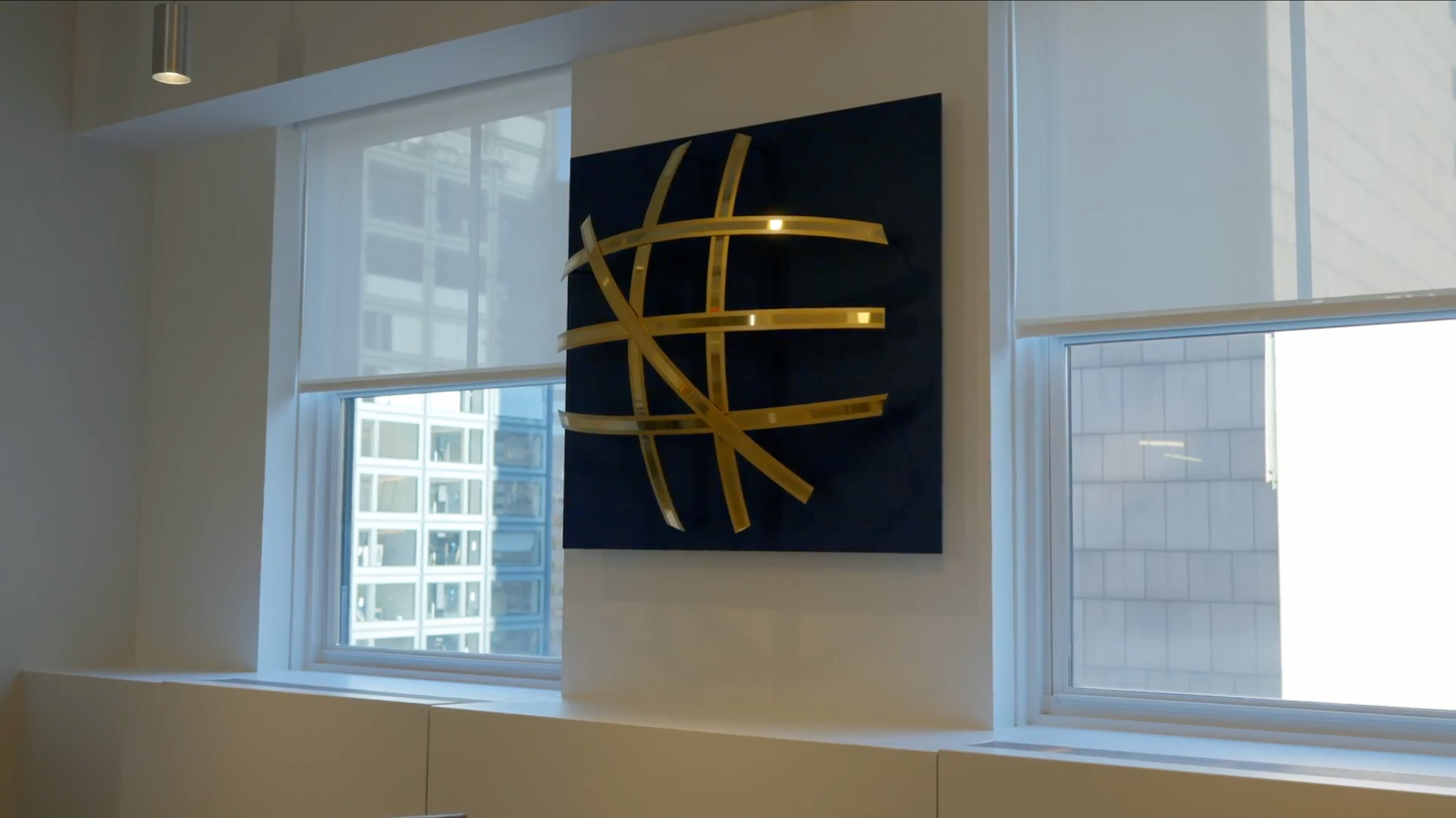 Gold abstract geometric wall art on a black square panel between two windows in a modern office.