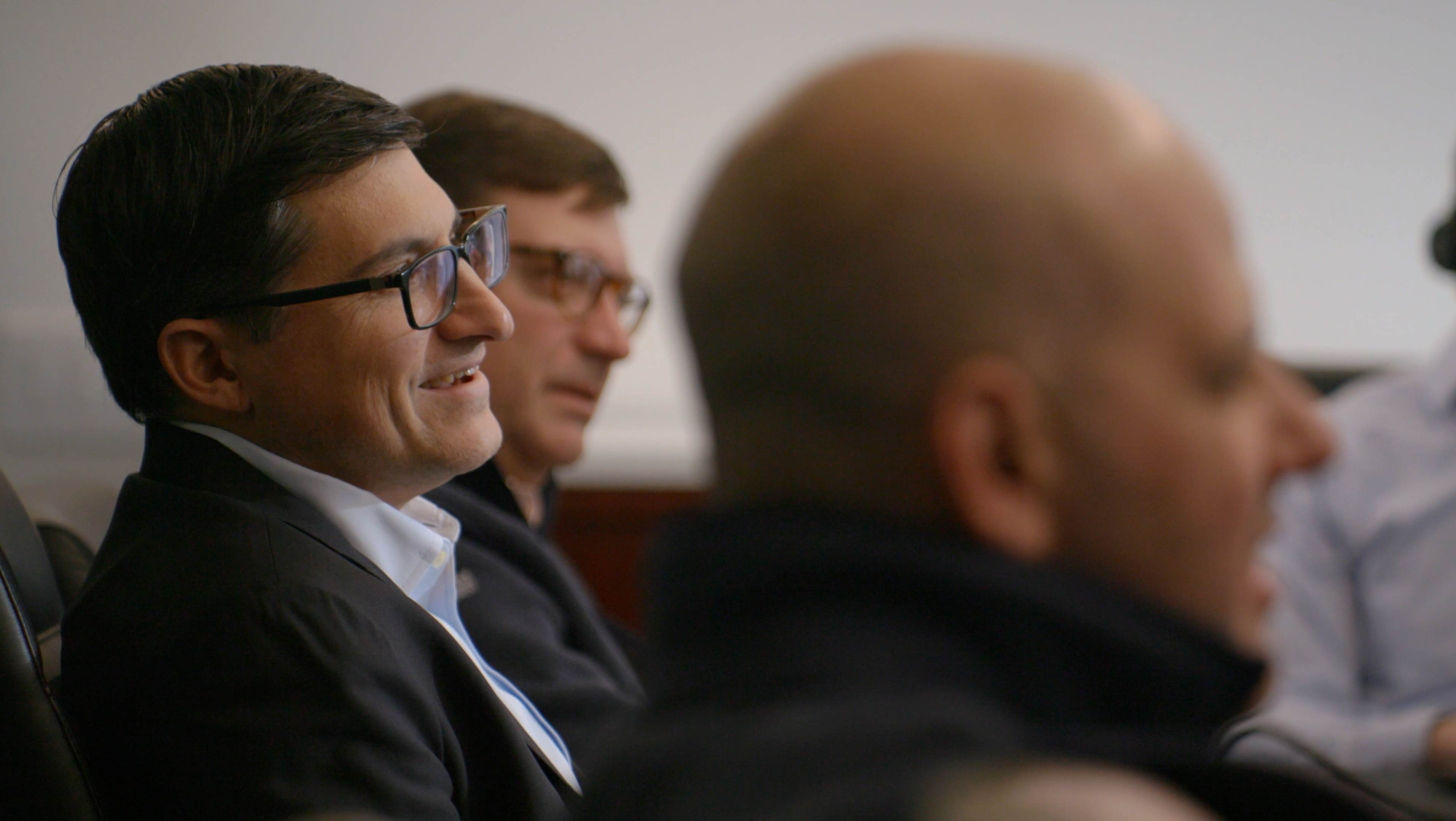 Three men sitting and listening during a meeting or discussion in an office setting.