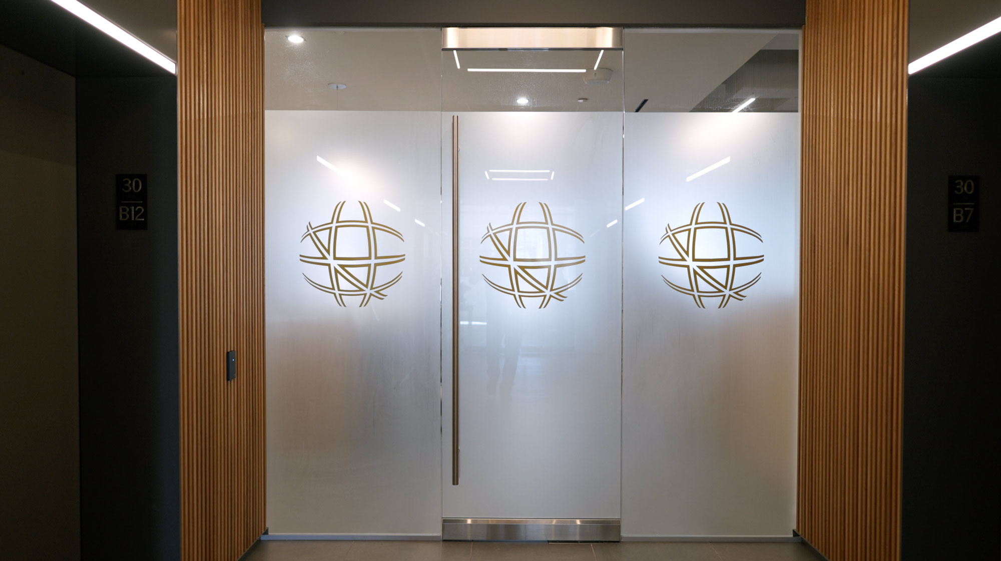 Frosted glass doors with three TSCM globe logos and wood panel walls on each side.