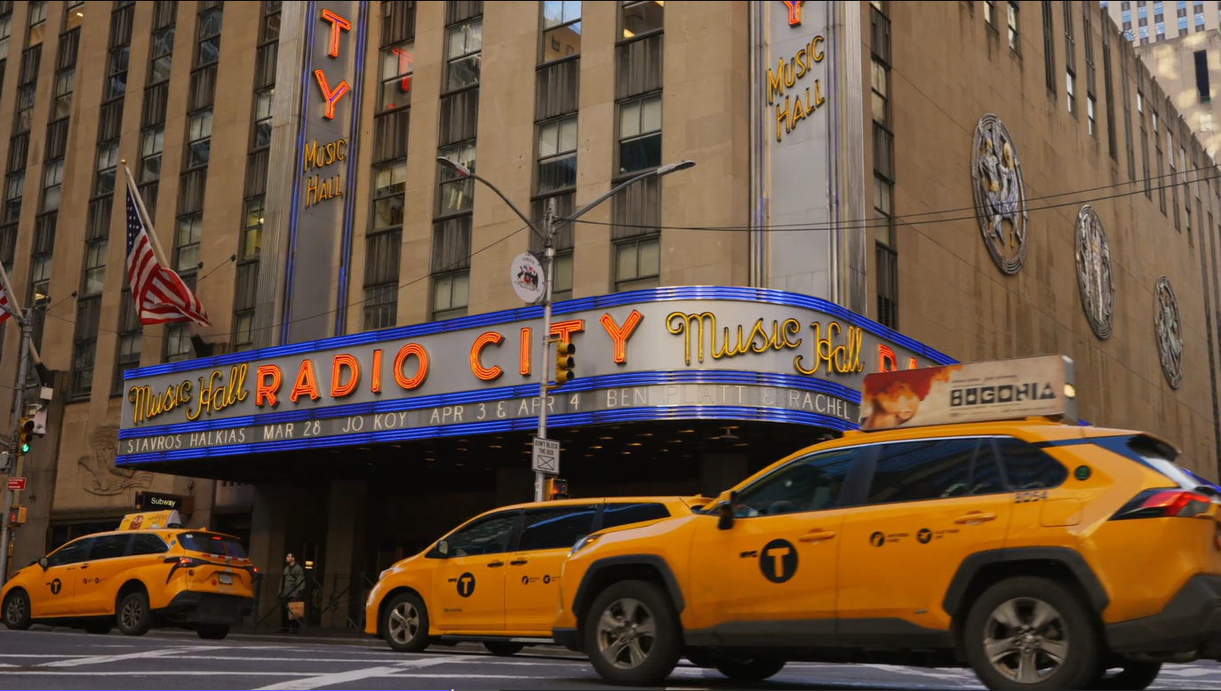 Radio City Music Hall marquee with New York yellow taxis driving past on the street.