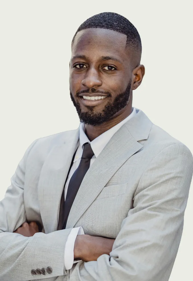 Confident man with short hair and beard wearing a light gray suit and black tie, smiling with arms crossed.