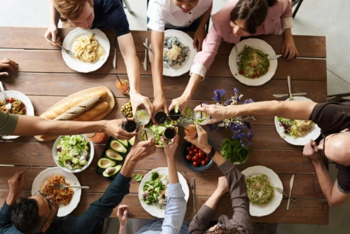 Top-down view of a family toasting drinks over a dinner table full of food, representing community and celebration.