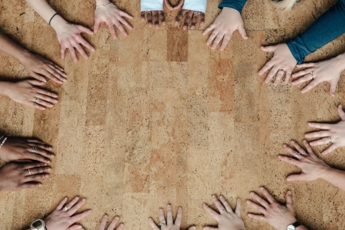 A circle of diverse hands resting on the floor, symbolizing unity, support groups, or community connection.