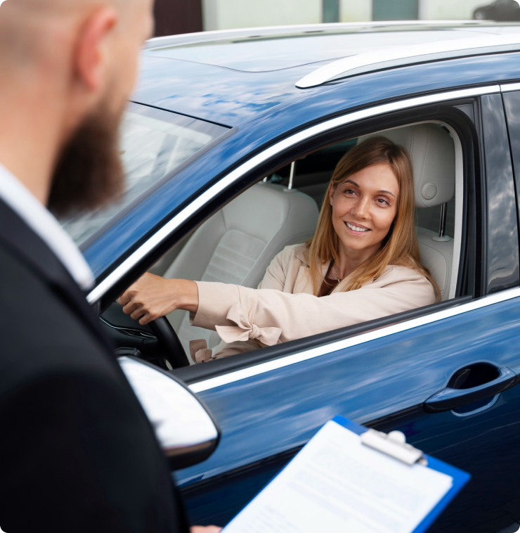 A smiling woman sitting in a blue car receiving paperwork from a dealership representative at a Las Vegas auto lot.