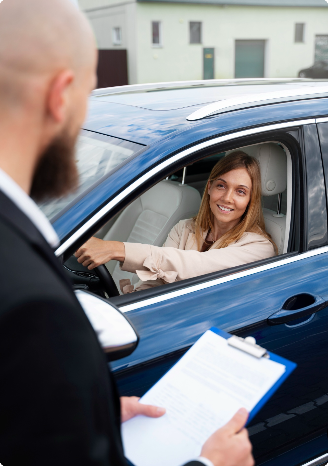 Car buyer in a blue SUV smiling while a dealership employee hands her paperwork during the vehicle purchase process.