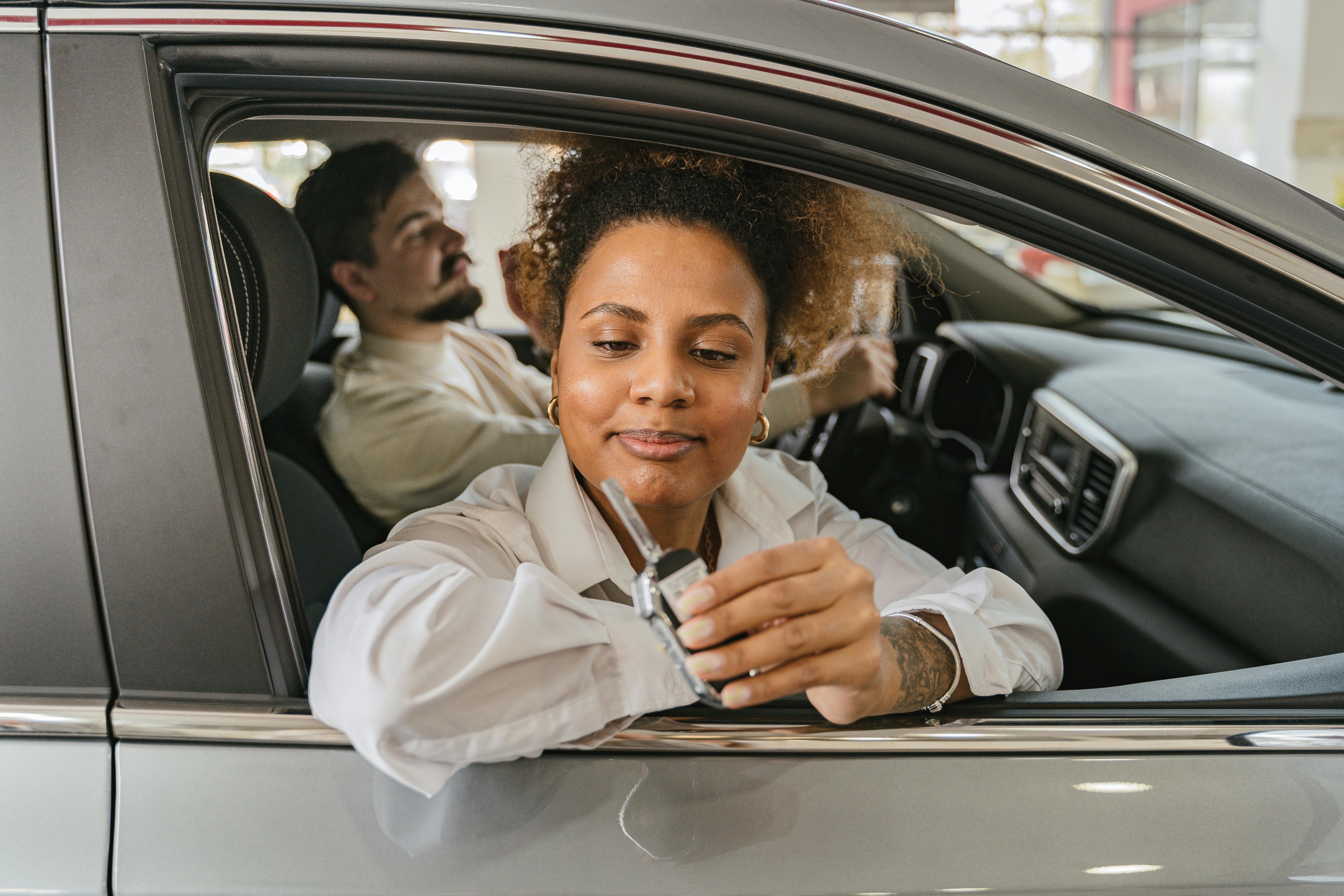 A woman sitting in the driver’s seat receives car keys while a man sits beside her inside a dealership, symbolizing a successful auto loan approval.