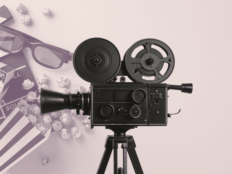 Gammel filmkamera på stativ med popcorn og briller ved siden av.