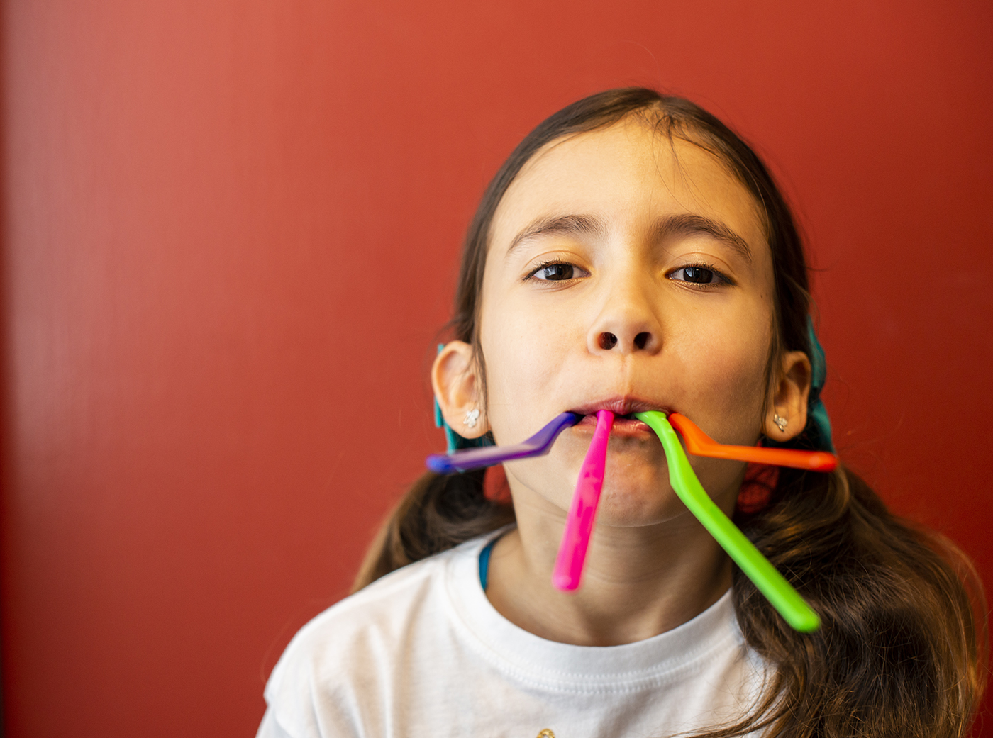 A young girl playing with colorful sticks between her teeth, around the age Phase I orthodontic treatment is considered