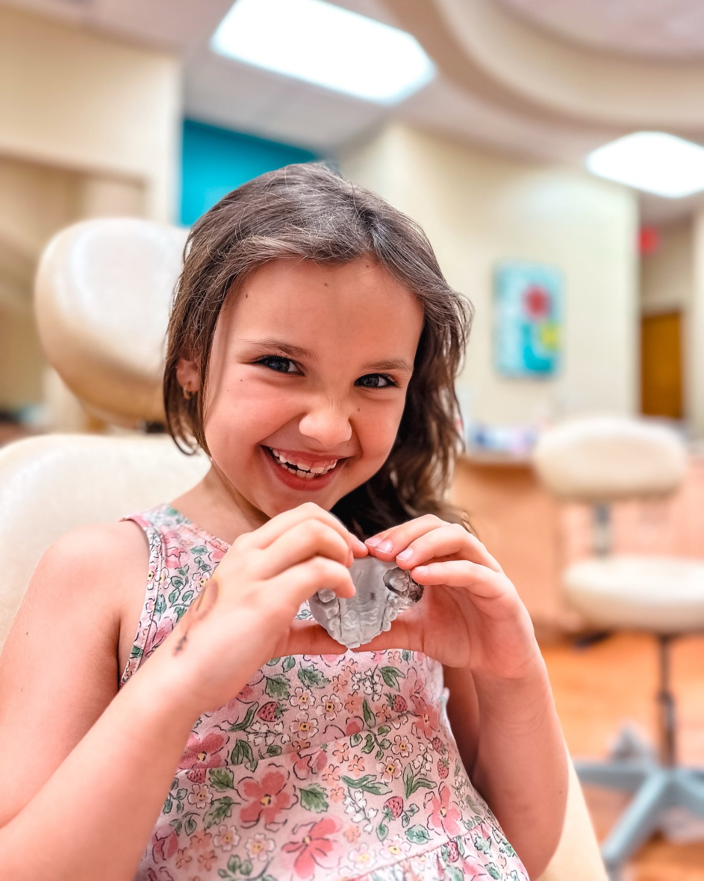 A young Ogden Orthodontics patient smiling and holding a Leaf palate expander
