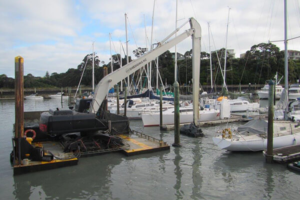 Long-reach excavator dredging alongside a marina berth