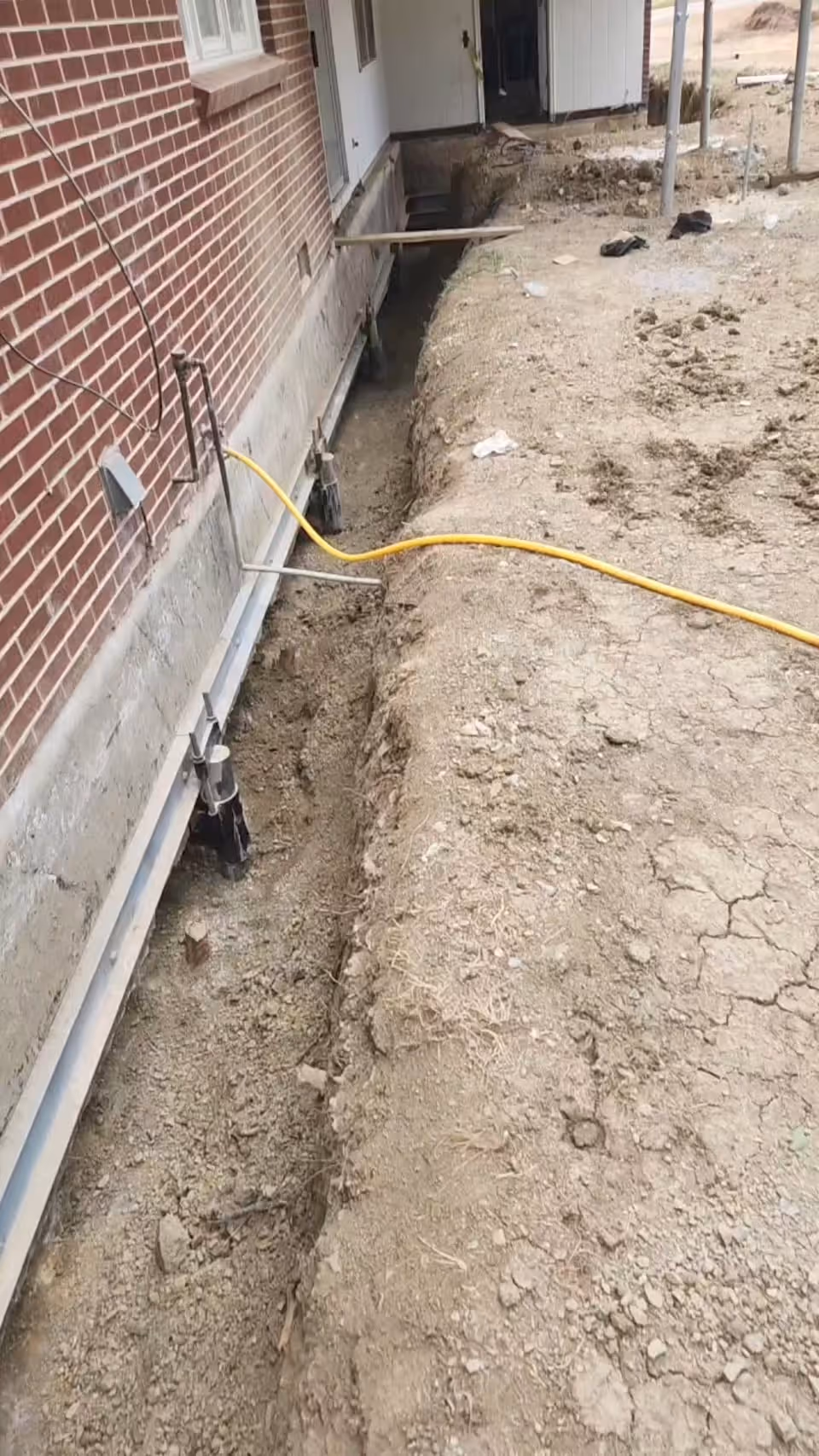 Construction site showing foundation repairs with steel supports and a trench dug alongside a brick building.