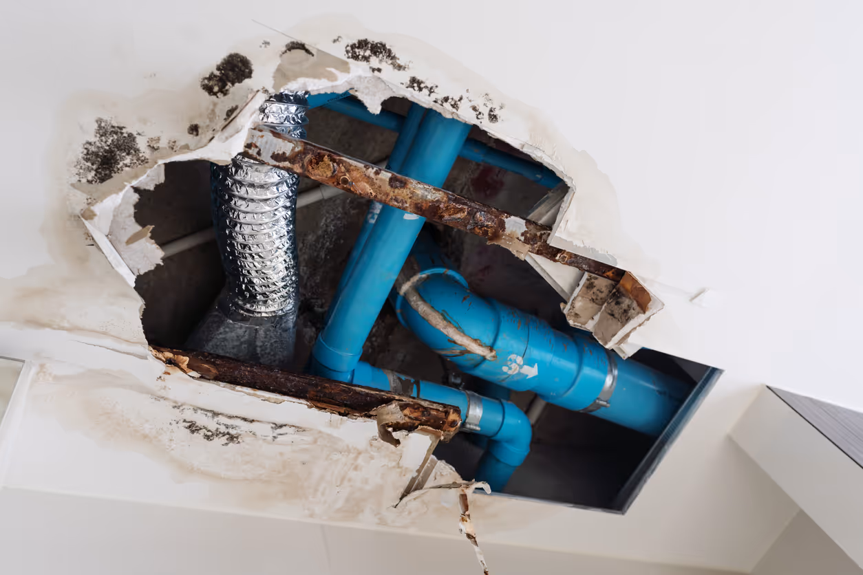 A hole in the ceiling showing various pipes that need repair.