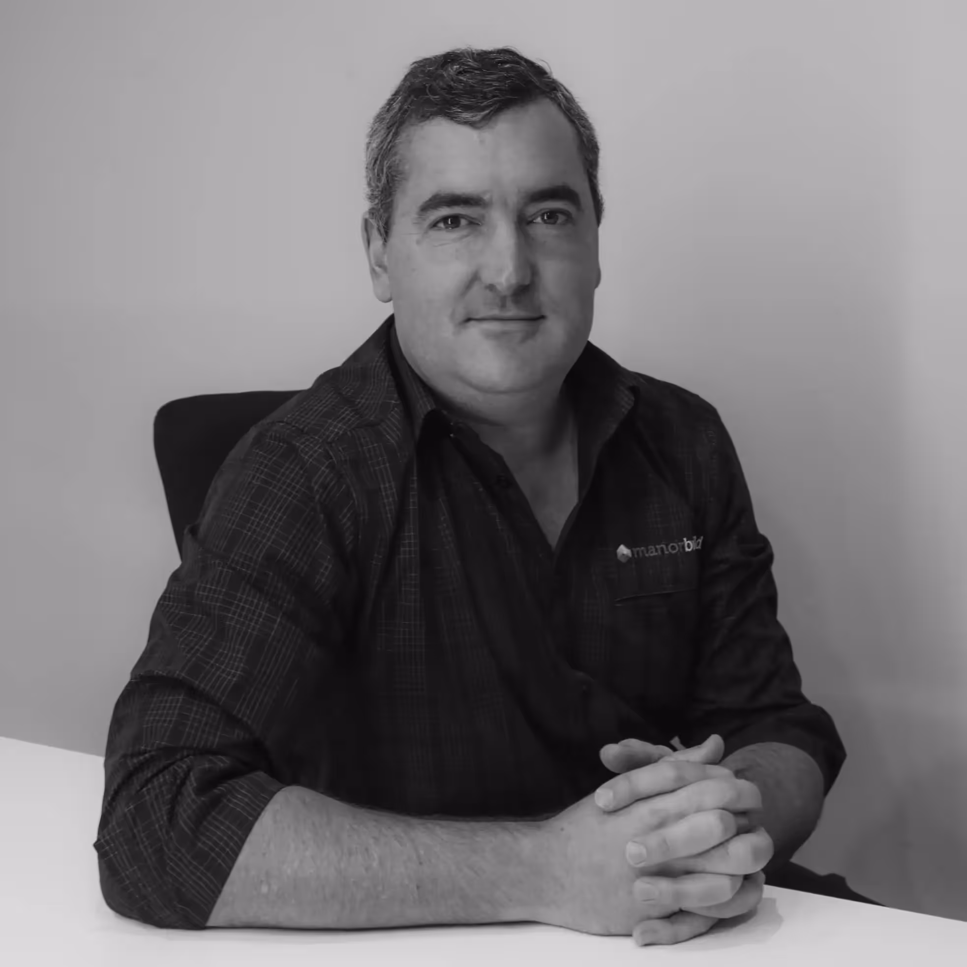 A black and white photo of a man with short hair. His arm rests on a table