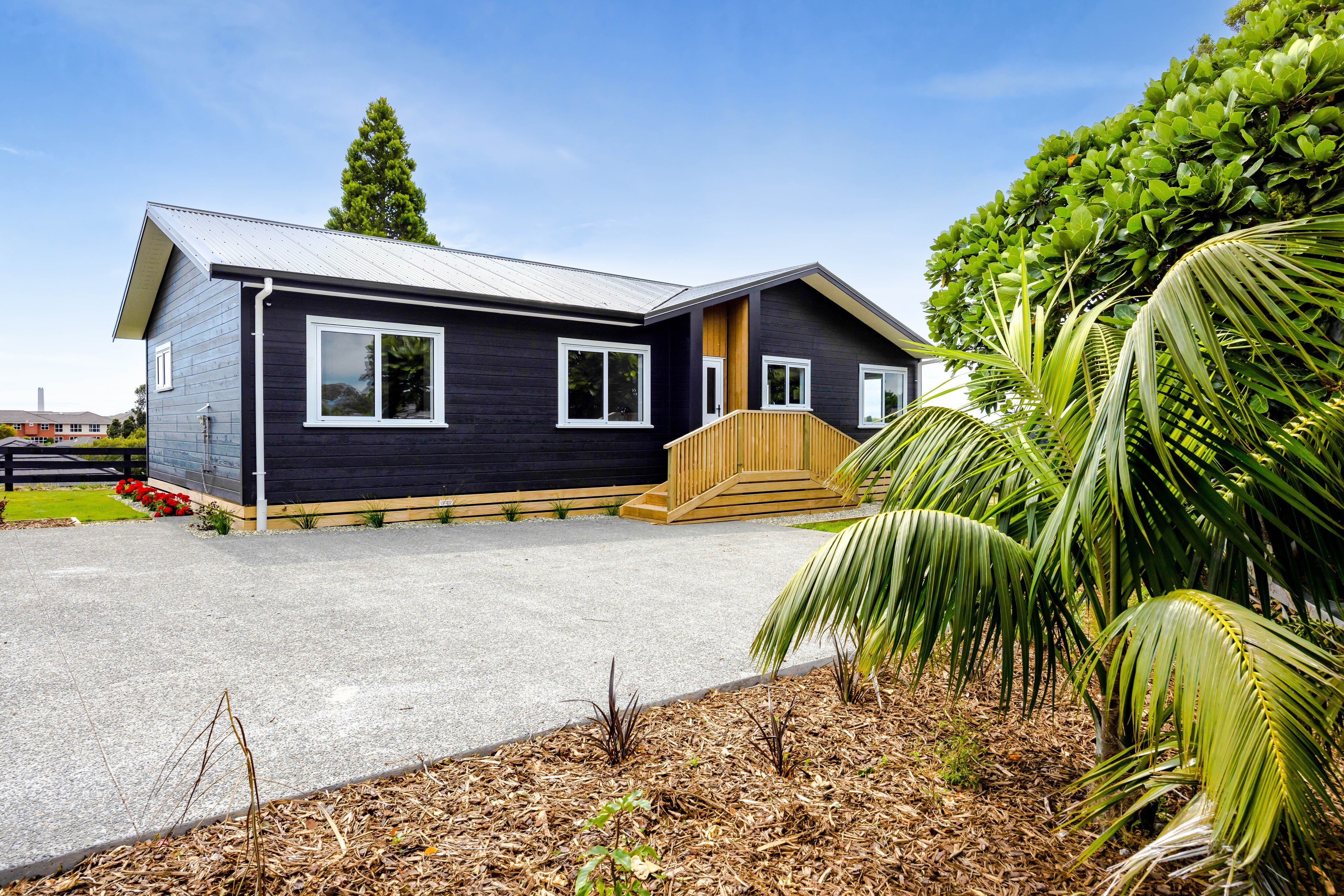 A modern looking black timber clad home with plants surrounding it.