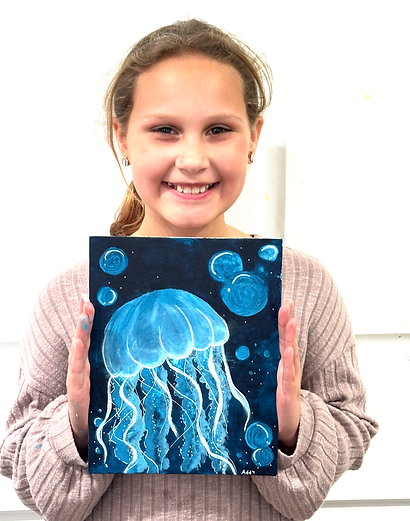 Smiling girl holding a painting of a glowing blue jellyfish on a dark background.