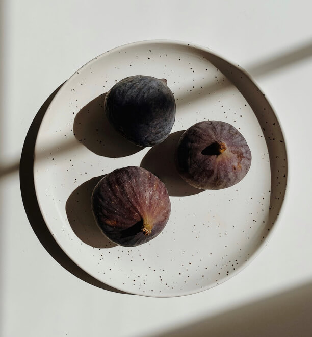 A ceramic plate with 3 purple figs inside.