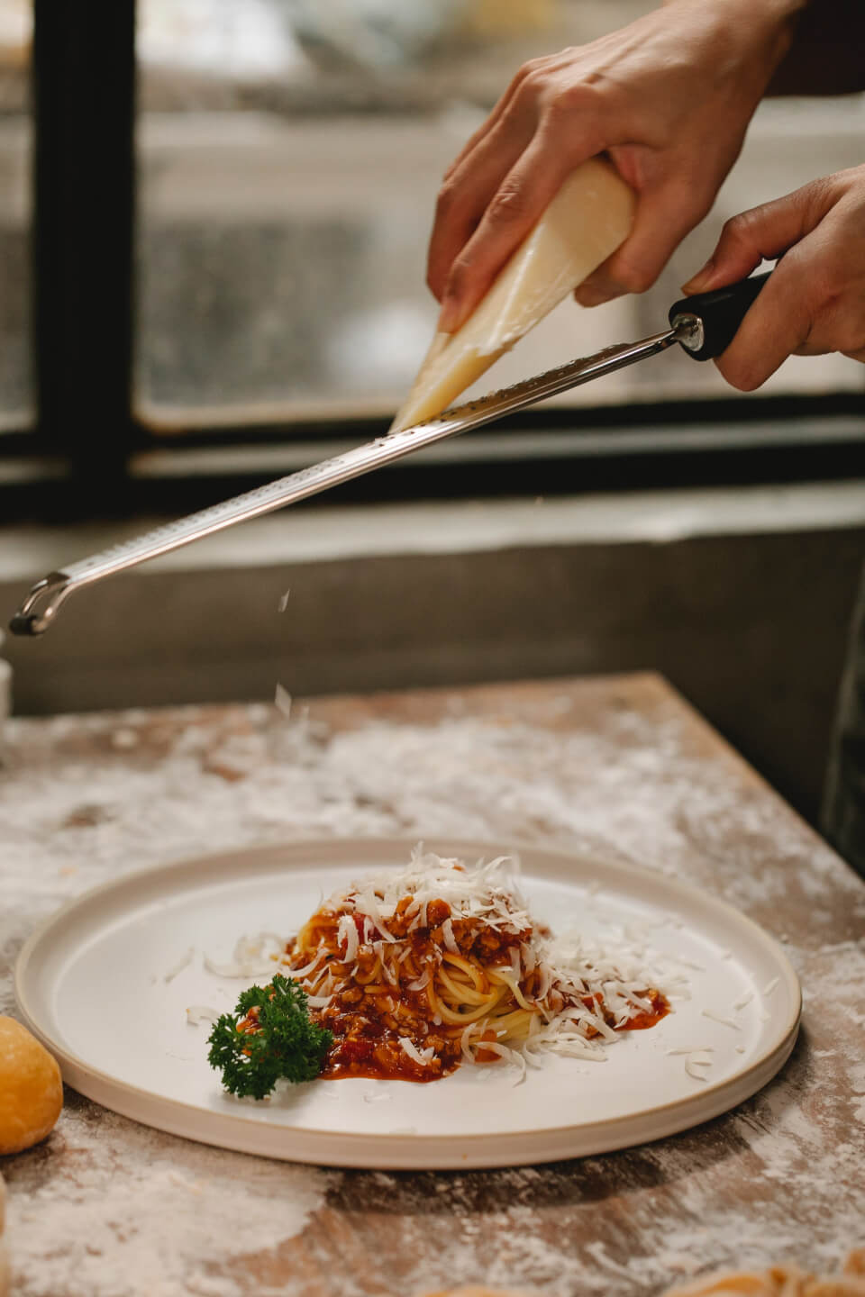 Hand grating parmesan cheese on top of a plate of spaghetti.