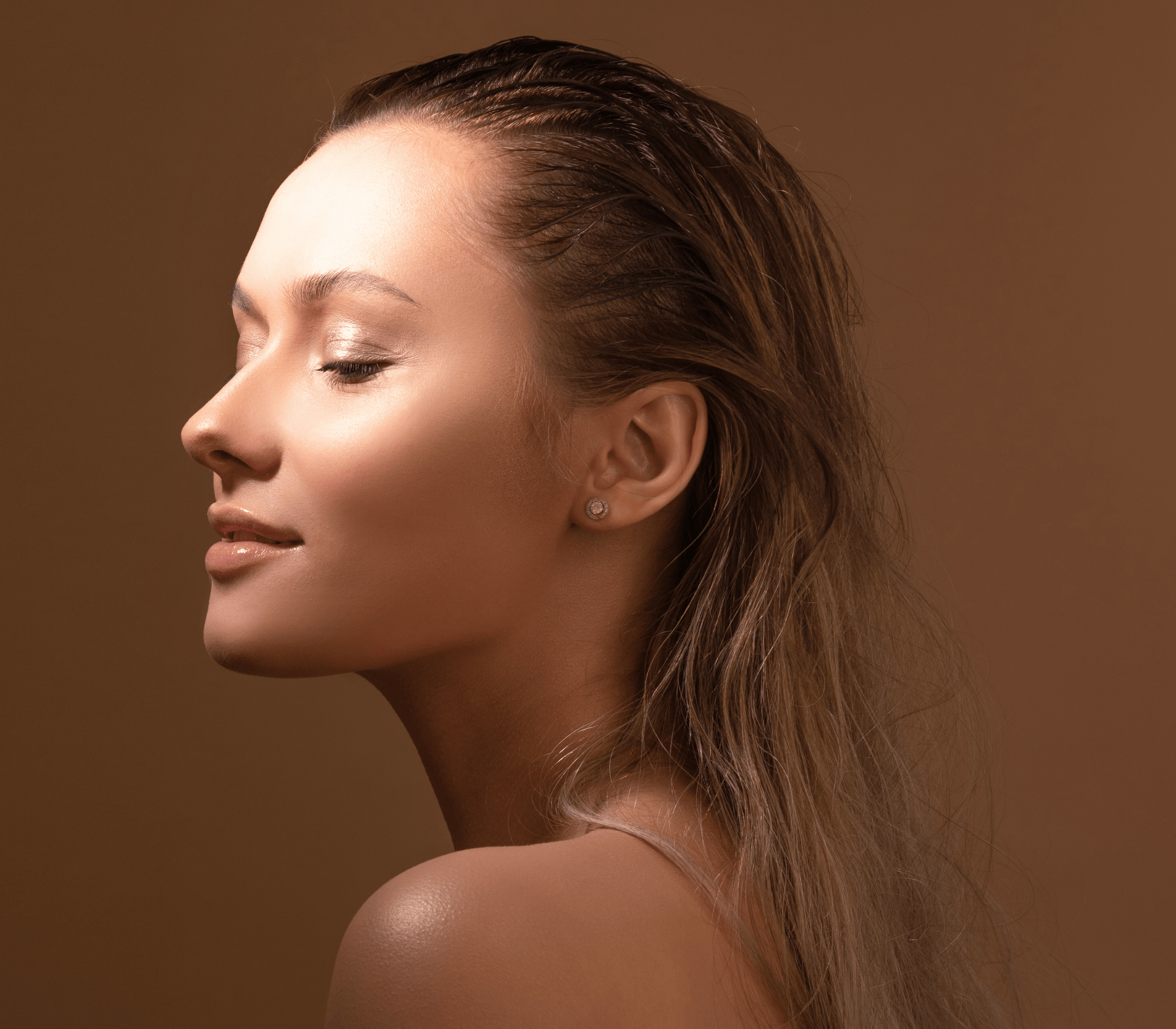 Side profile of a serene woman with wet hair and closed eyes against a brown background posing for TANNED TO - Automated spray tan service in Toronto.