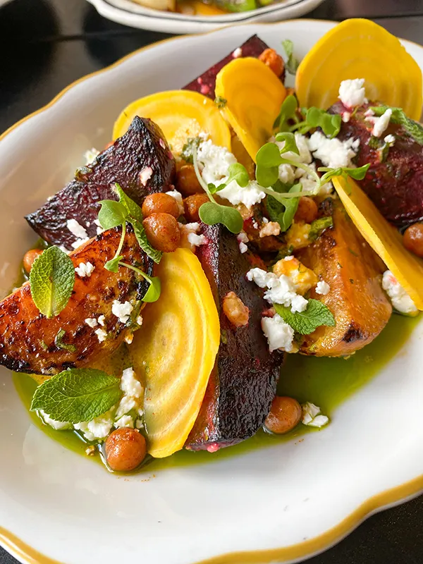 Assiette de légumes rôtis colorés avec des tranches de betterave jaune, des morceaux de betterave rouge, des pois chiches grillés, du fromage émietté et des feuilles de menthe.