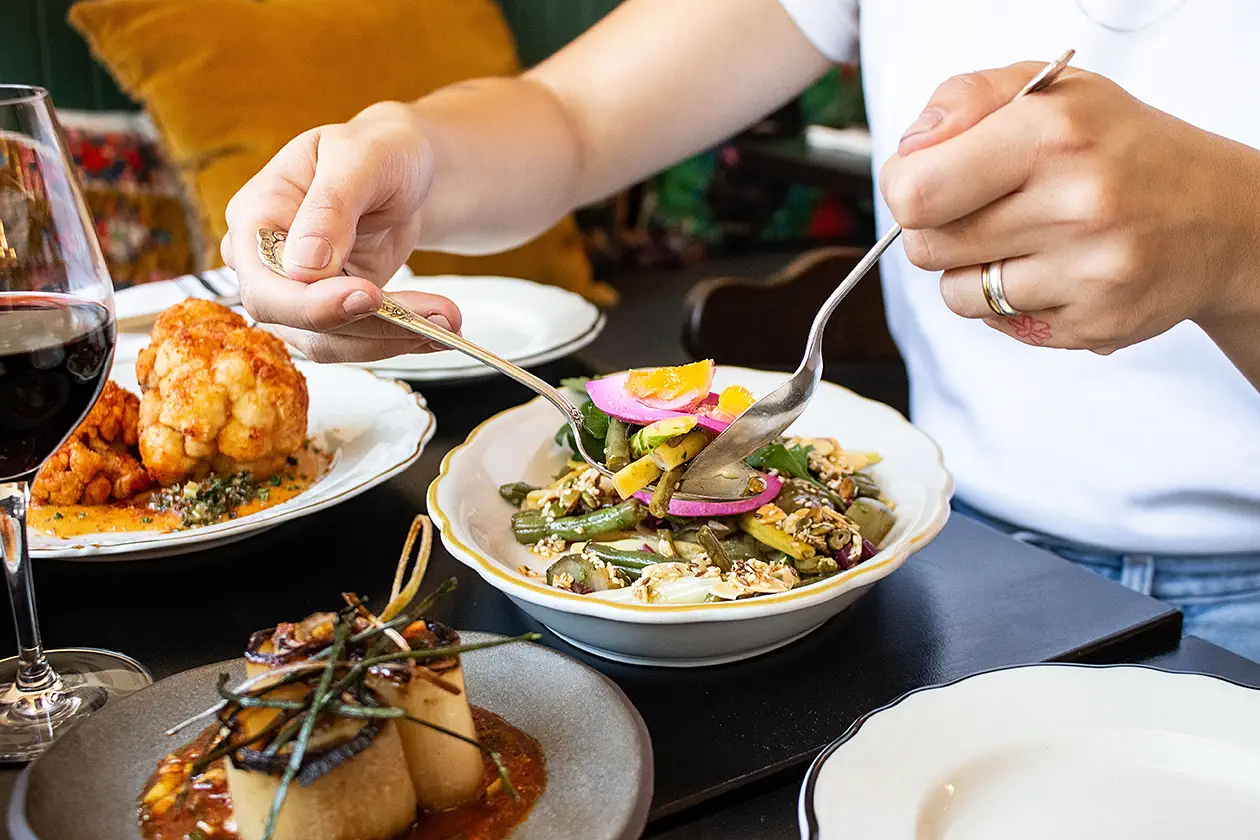 Personne utilisant une fourchette et une cuillère pour manger une salade de haricots verts avec oeufs et divers granitures