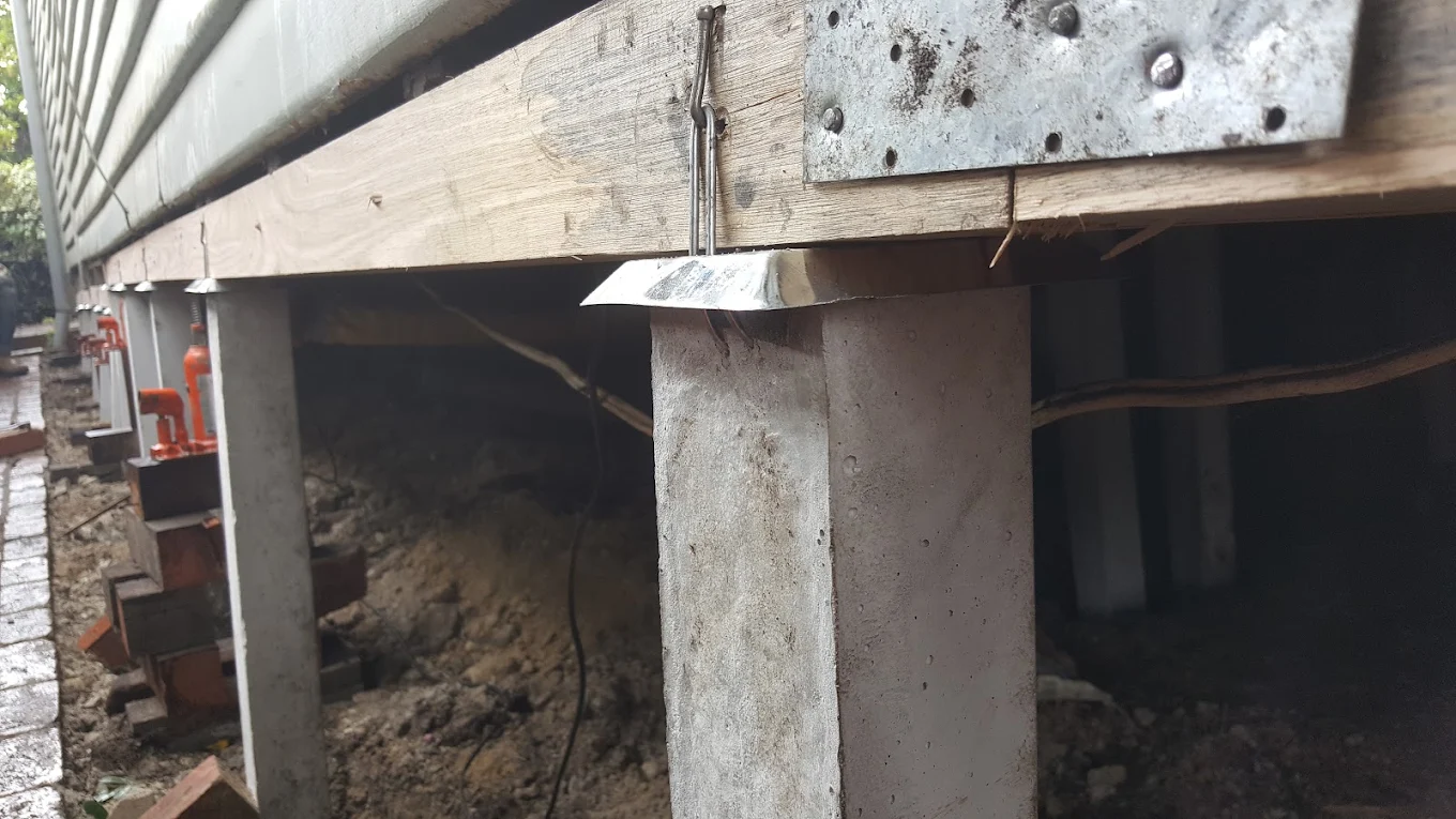 Concrete foundation posts supporting a wooden deck frame with metal brackets and clips, viewed from underneath.