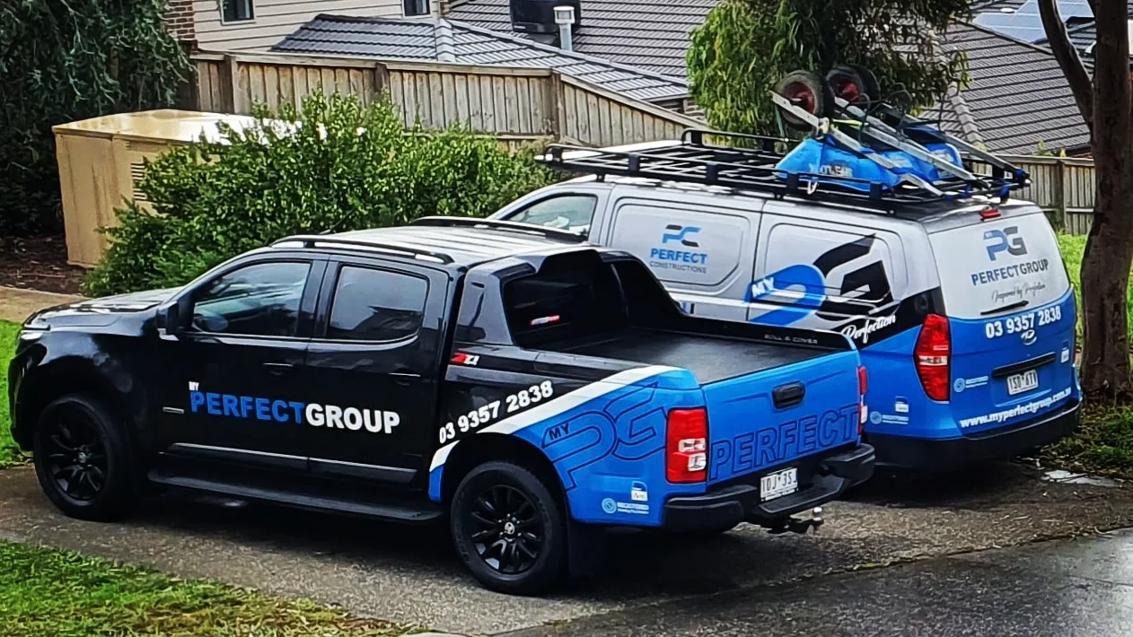 Two vehicles parked side by side with MY PERFECT GROUP branding, including a pickup truck and a van with roof racks carrying equipment.