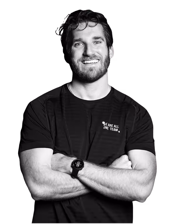 Smiling man with beard and wavy hair, wearing a black t-shirt and wristwatch, arms crossed.