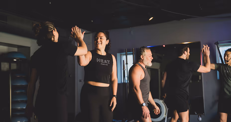 Two pairs of people in workout clothes giving each other high-fives in a gym setting.