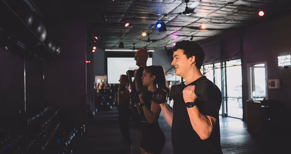 Group of people lifting dumbbells in a dimly lit gym during a workout class.