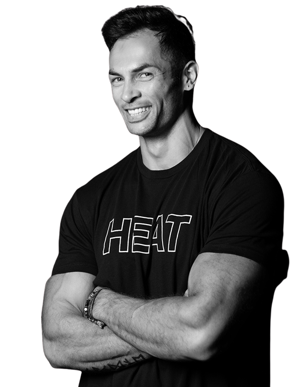 Smiling muscular man with short dark hair wearing a black t-shirt with the word 'HEAT', arms crossed.