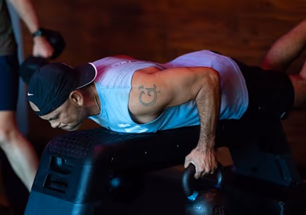 Man wearing a backwards cap performing a push-up with hands on kettlebells in a gym setting.