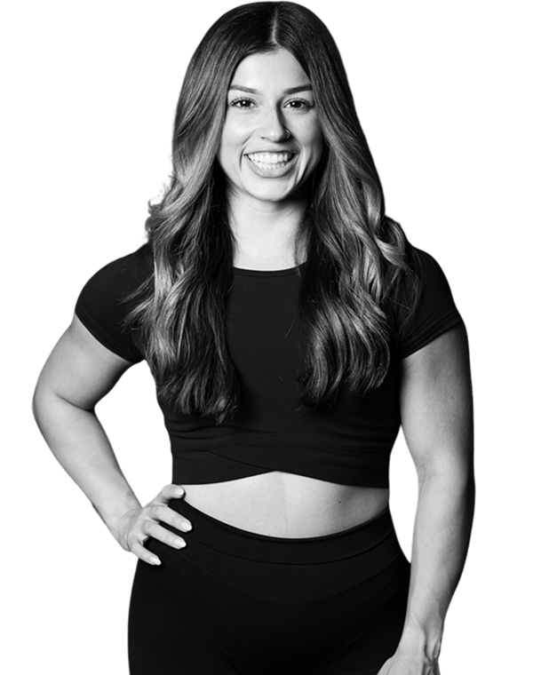 Smiling woman with long wavy hair wearing a black crop top and black leggings, standing with one hand on her hip.