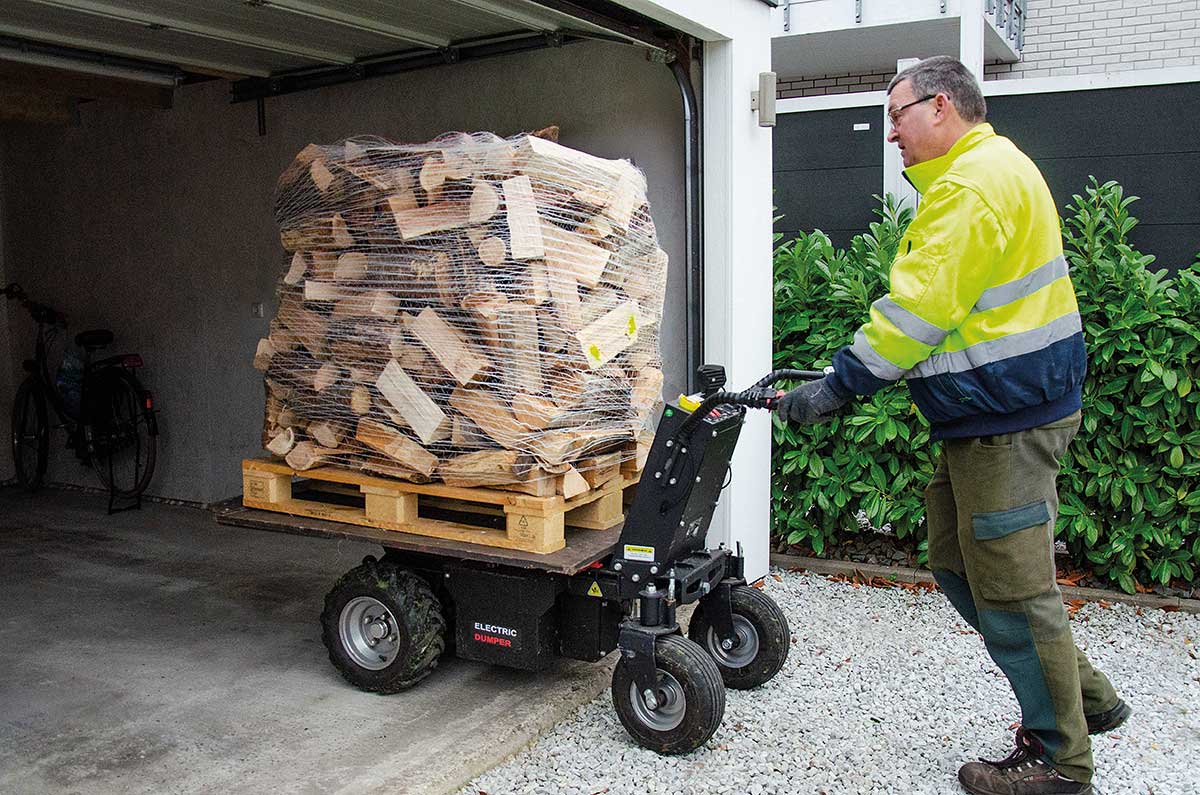 Mann transportiert Kaminholz auf elektrischem Transportgerät vor Garage.