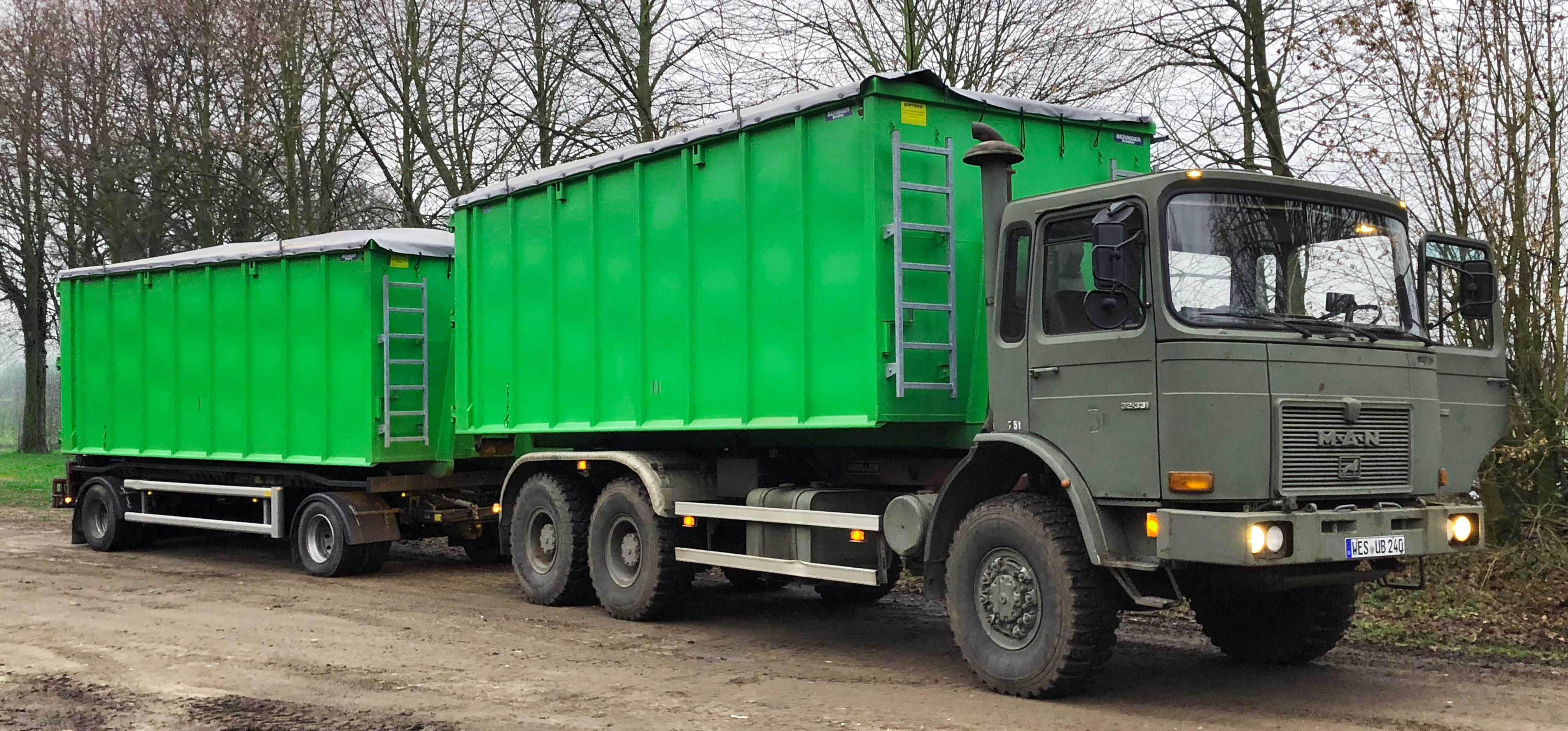 Großer Militär-LKW mit grünen Anhängern parkt auf einem schmutzigen Weg im Wald.