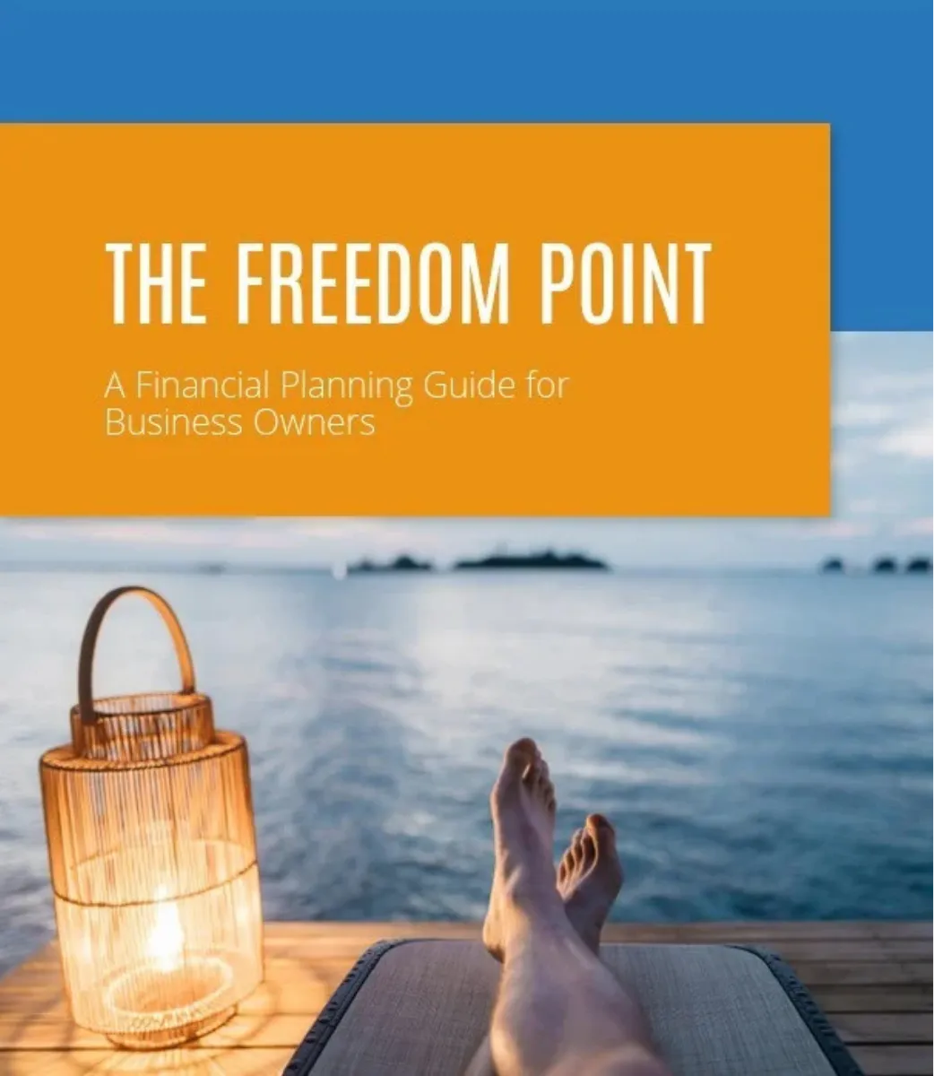 View of a person's legs resting on a lounge chair by the water at sunset with a lit lantern nearby and text overlay reading 'The Freedom Point: A Financial Planning Guide for Business Owners'.