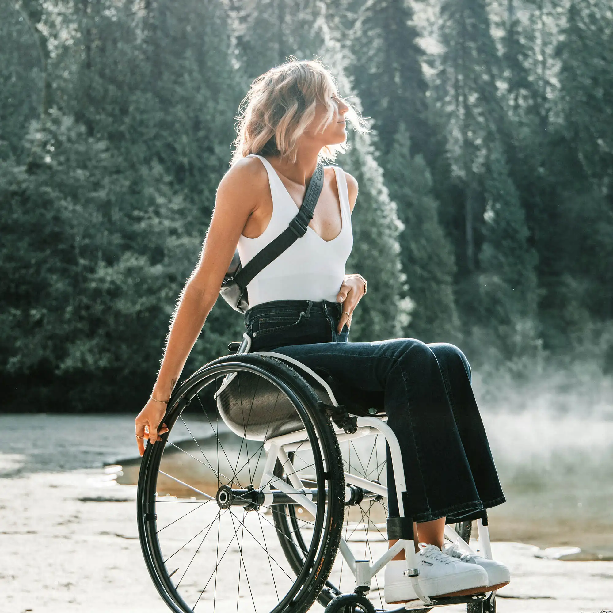 Barrierefreies Reisen: Eine Frau im Rollstuhl steht an einem Seeufer, im Hintergrund Bäume